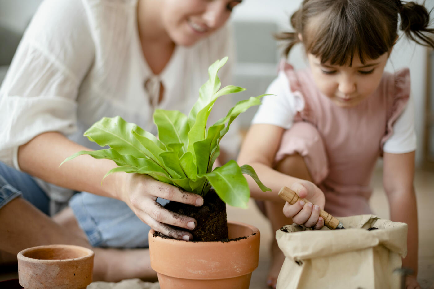 Un adulte et un enfant utilisent du compost pour rempoter une plante en pot.